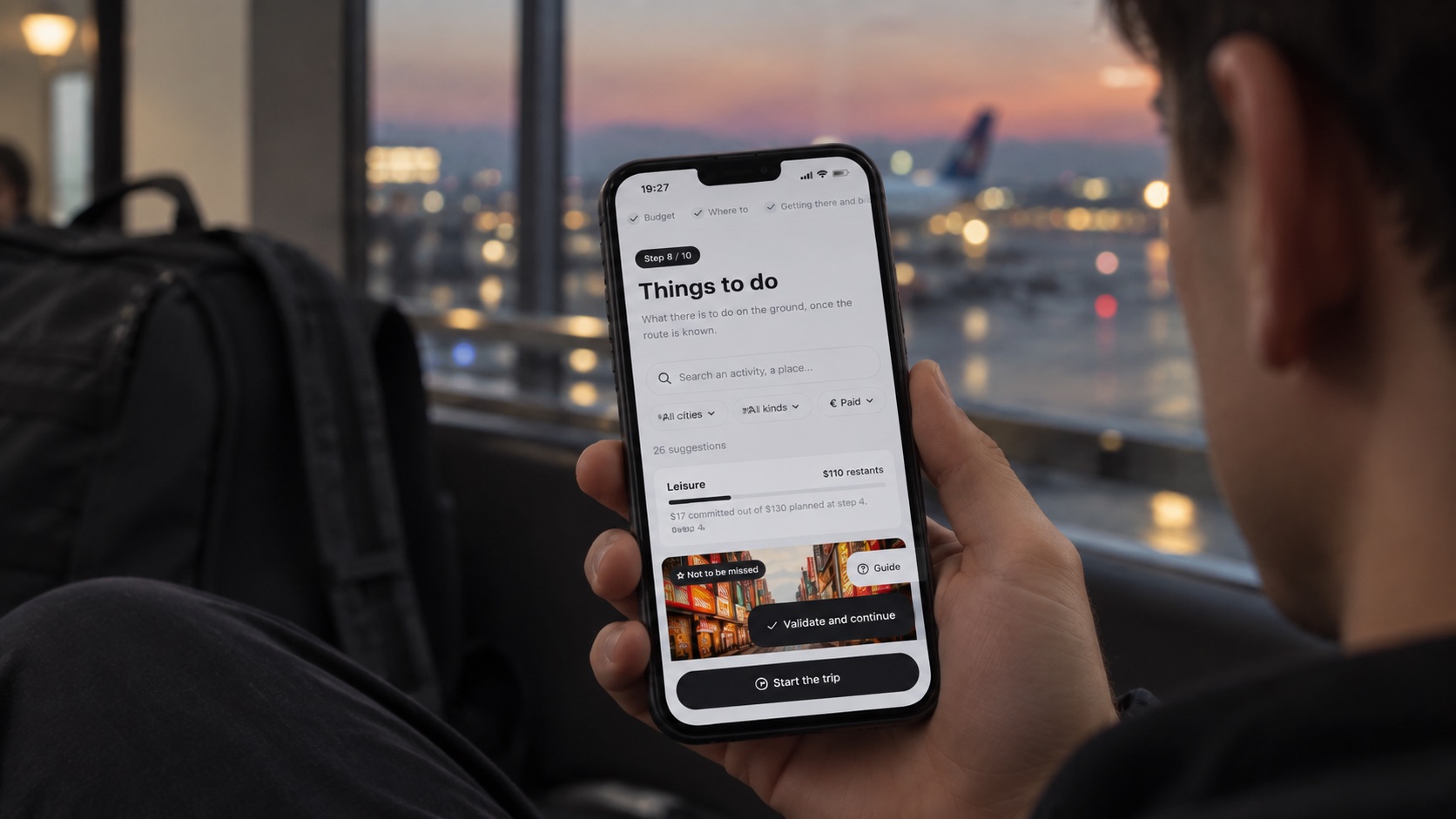 A traveller uses REVENTURY Travel Planner on their phone at the airport at sunset.